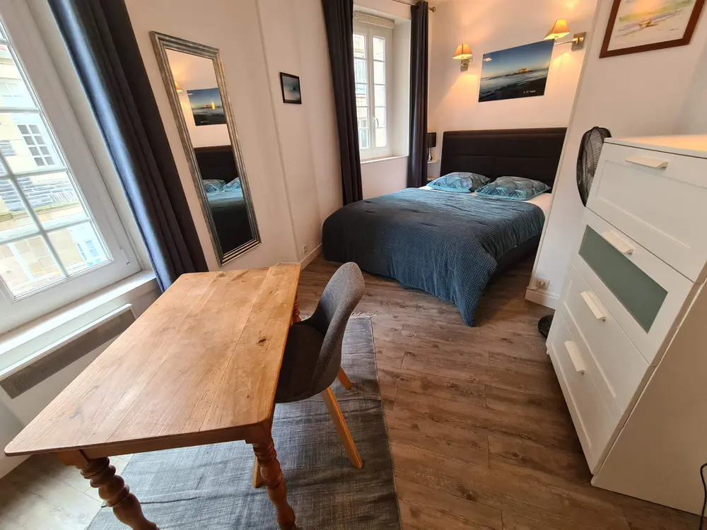 La chambre avec un lit double, un bureau en bois et deux fenêtres