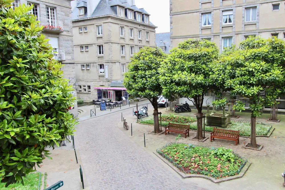 Vue depuis la fenêtre sur la place arborée et fleurie